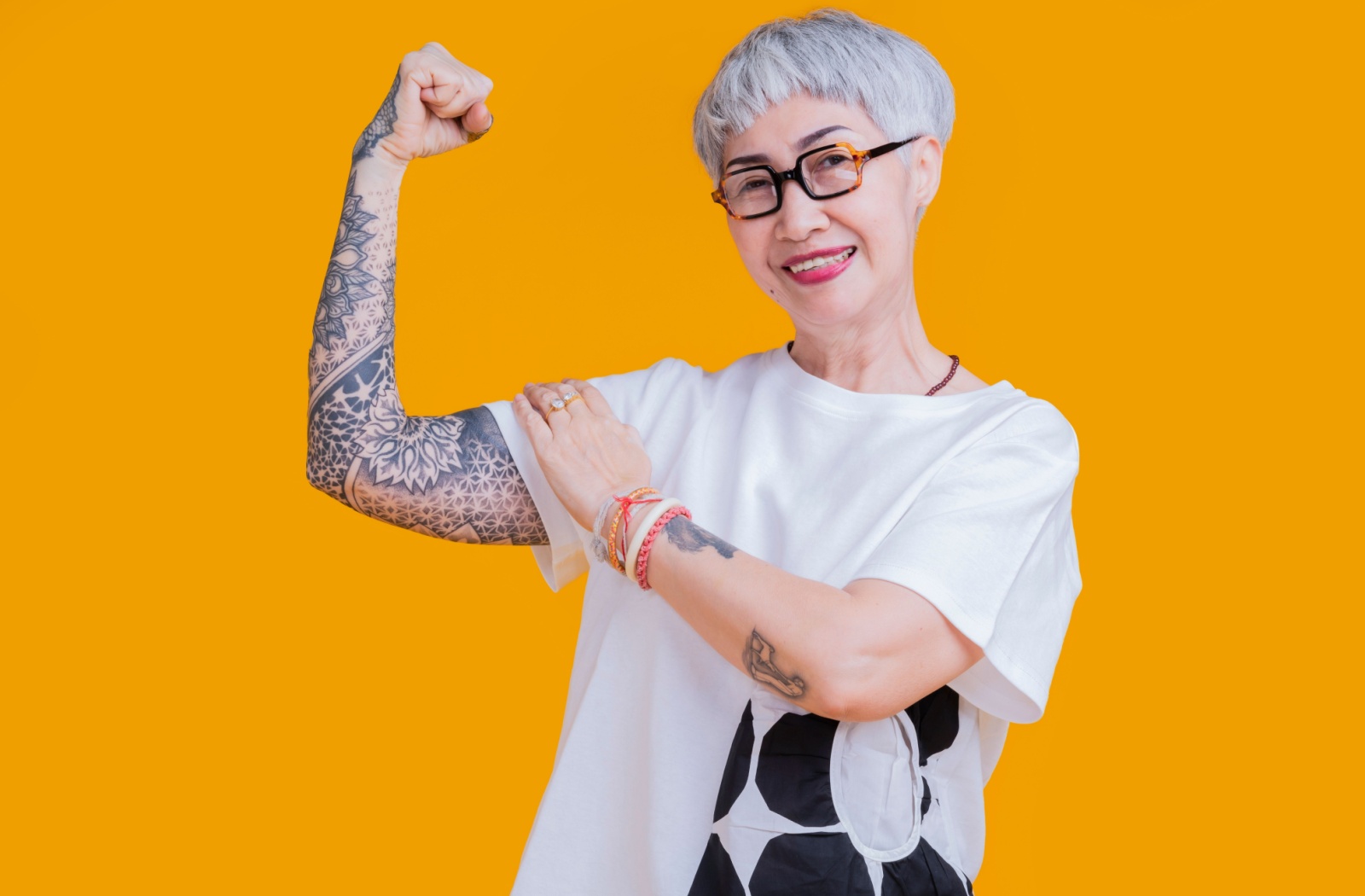A senior with a full arm sleeve tattoo poses against a mustard yellow backdrop.