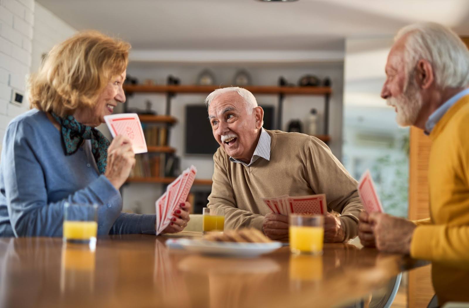 A group of senior friends play a game of cards over breakfast and orange juice