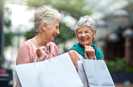 two senior friends smile while holding shopping bags